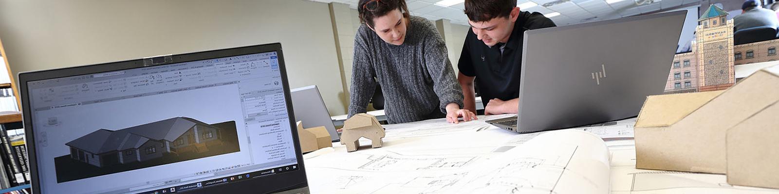 Students reviewing blueprints on table with design software and models